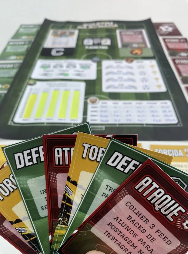 Tabuleiro em formato de campo de futebol e cartas de ataque, defesa e torcida da Copa dos Campeões.